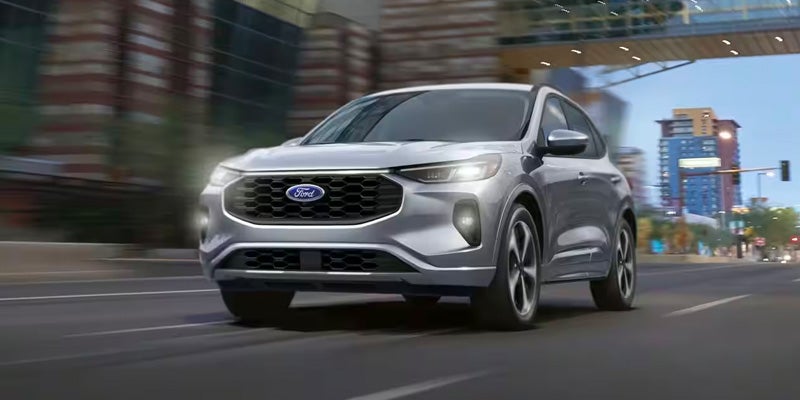 Silver Ford Escape SUV driving on a city street with headlights on and motion blur in the background.