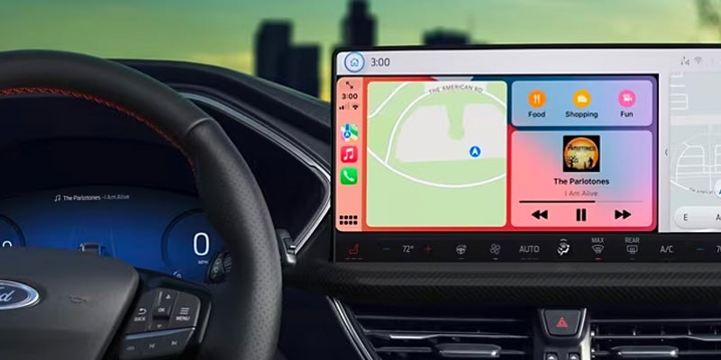 Car interior with a steering wheel, digital dashboard, and a large infotainment screen showing Apple CarPlay with map, music, and apps.