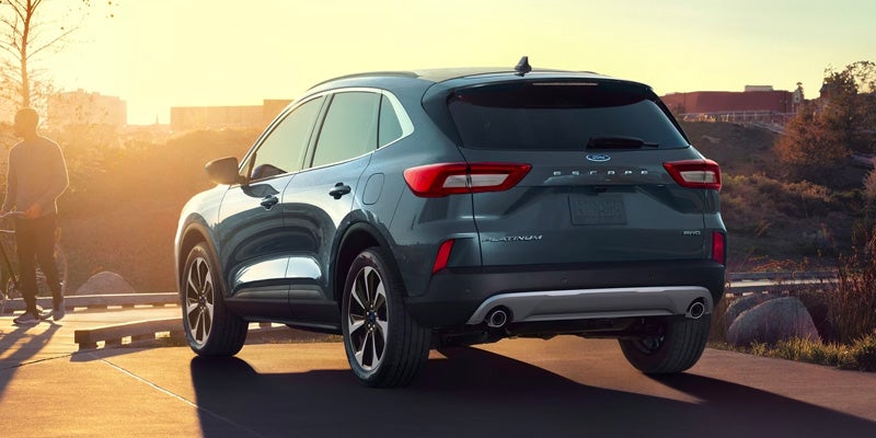 Dark blue Ford Escape Platinum SUV seen from the rear-right at sunset, with a person and bicycle on the left.