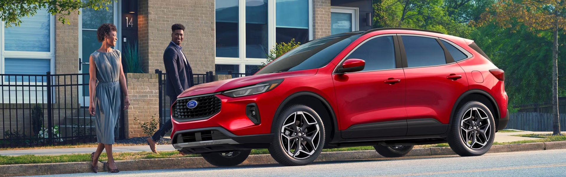 Red Ford Escape SUV parked on a street with a smiling man and woman walking towards it from a modern home.