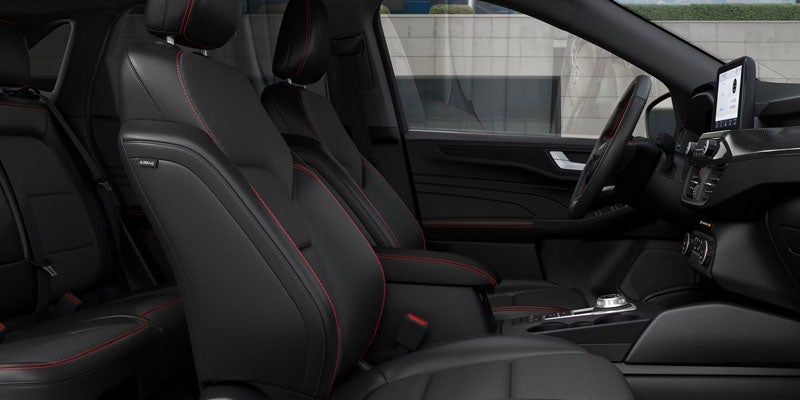Car interior with black leather seats and red stitching, dashboard, steering wheel, and infotainment screen.