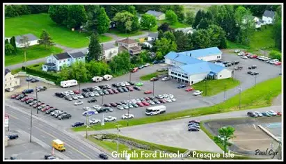 Aerial view of Griffeth Ford Lincoln car dealership in Presque Isle with blue roofs, large parking lots, and many vehicles.