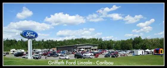 Griffeth Ford Lincoln dealership with a large lot full of cars, a Ford sign, and a bouncy castle under a blue sky.